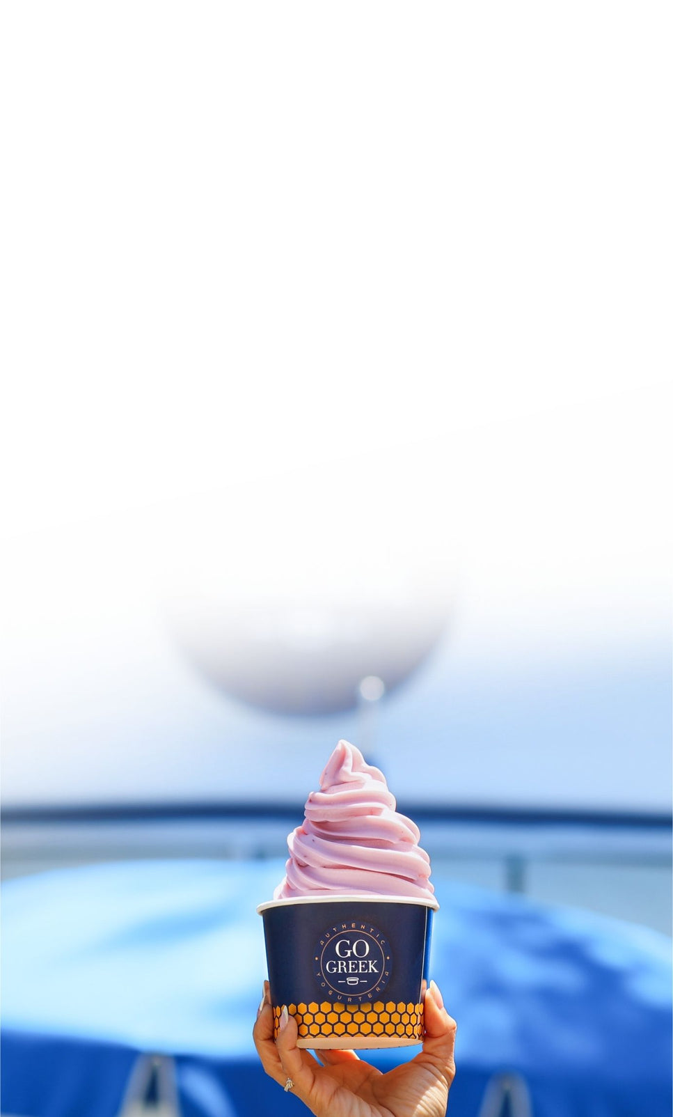 cup of black currant go greek yogurt in a logo cut being held outside of the storefront