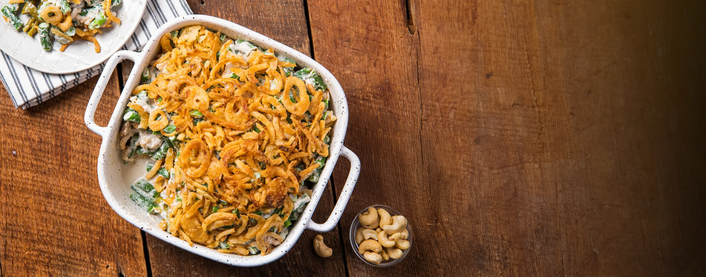 Green bean casserole with fried onions in a white dish on a wooden table
