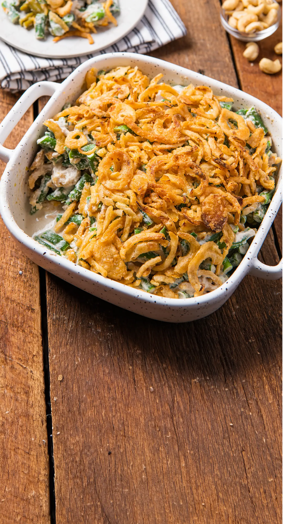 Green bean casserole with fried onions in a white dish on a wooden table