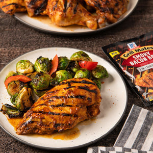 A plate of grilled chicken breast with brussels sprouts and a package of Grill Mates Smoky Bacon BBQ seasoning.