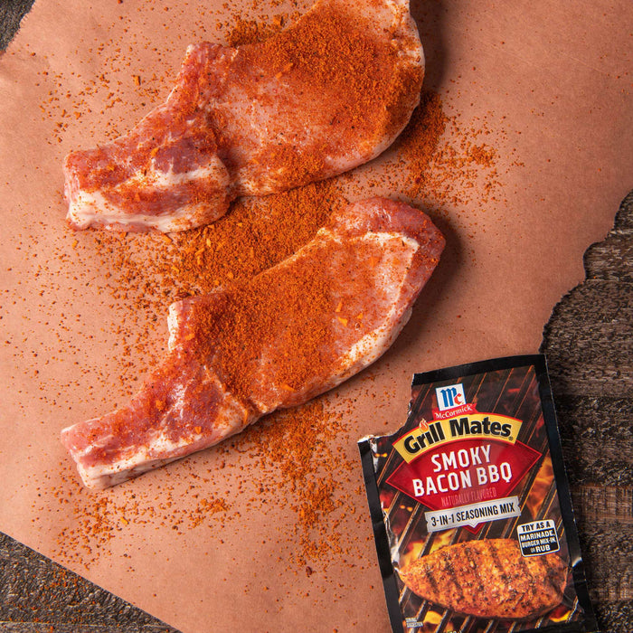 Two pieces of raw pork are seasoned with McCormick Grill Mates Smoky Bacon BBQ seasoning.