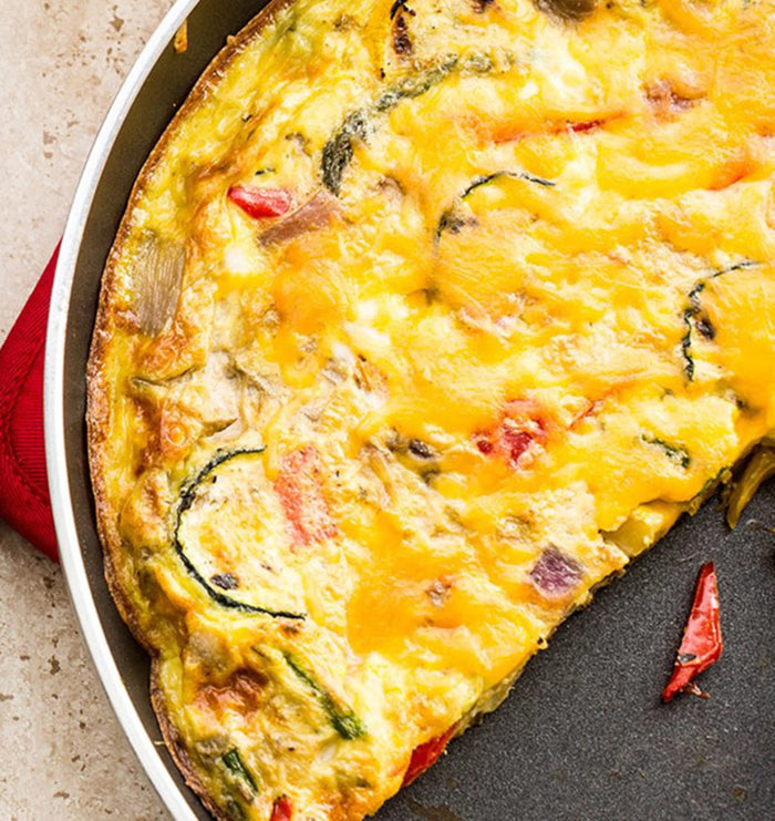 A close-up of a cheesy omelet with vegetables in a skillet.