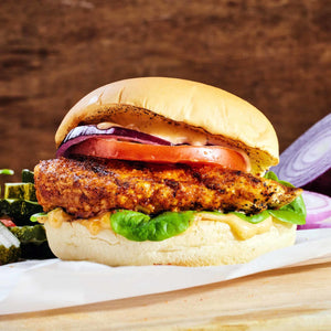 A close-up of a chicken burger with lettuce, tomato, red onion, and a creamy sauce.