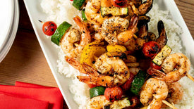 Shrimp skewers with vegetables on a bed of rice on a white plate.