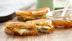 Grilled cheese sandwich cut in half on a wooden table with a side of jelly.