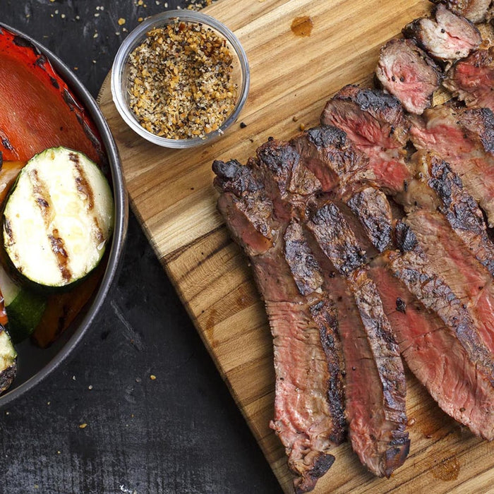 Grilled steak sliced on a wooden cutting board with a side of grilled zucchini and peppers.