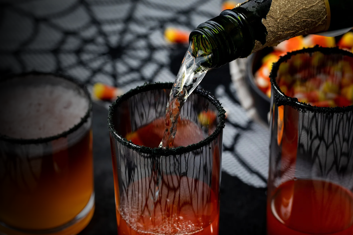 Halloween-themed cocktail being poured into a glass with a spider web background.