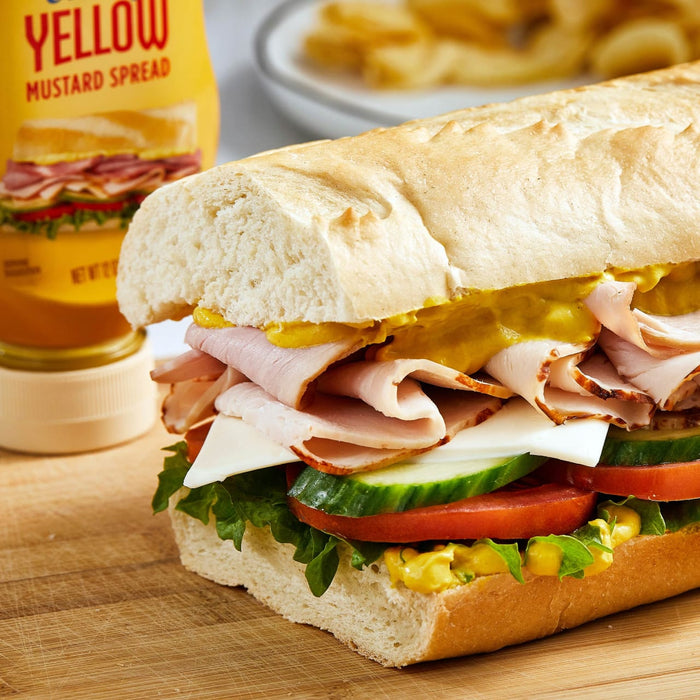 A turkey sandwich with yellow mustard spread on a wooden cutting board.