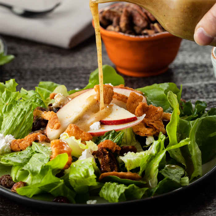 A salad with apple slices, lettuce, and a honey mustard dressing being poured over it.