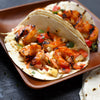 A close-up of a shrimp taco with grilled shrimp, cabbage, and other vegetables.