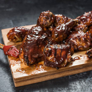A close-up of a wooden cutting board with a pile of barbecued chicken pieces.