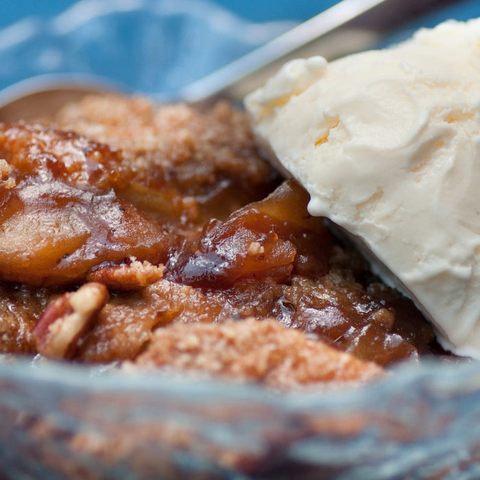 A close-up of a bowl of apple crisp with a scoop of vanilla ice cream on top.