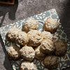 A collection of round cookies coated in a fine dusting of powdered sugar and spices are arranged on a decorative patterned plate.
