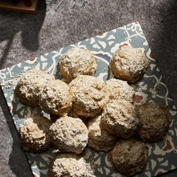 A collection of round cookies coated in a fine dusting of powdered sugar and spices are arranged on a decorative patterned plate.