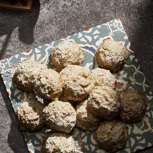 A collection of round cookies coated in a fine dusting of powdered sugar and spices are arranged on a decorative patterned plate.
