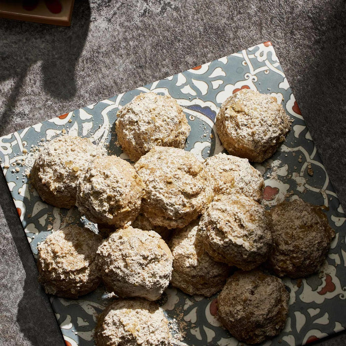 A collection of round cookies coated in a fine dusting of powdered sugar and spices are arranged on a decorative patterned plate.