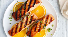 Grilled salmon with orange slices on a white plate