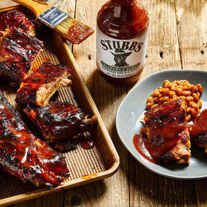 A bottle of Stubbs Jalapeno &amp; Honey BBQ Sauce next to a plate of baked beans and ribs.