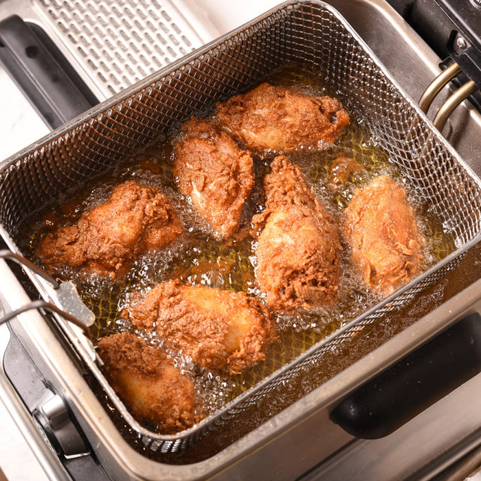 A deep fryer with chicken pieces frying in hot oil.