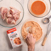 A hand dips a piece of chicken into a bowl of Zatarains New Orleans Style Hot &amp; Spicy Chicken Fry Mix.