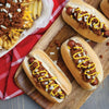 Three hot dogs with chili and mustard on a wooden cutting board.
