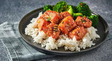 Plated dish of rice with teriyaki chicken and broccoli on a gray surface.