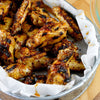 A close-up of a metal pan with a white paper liner filled with grilled chicken wings.