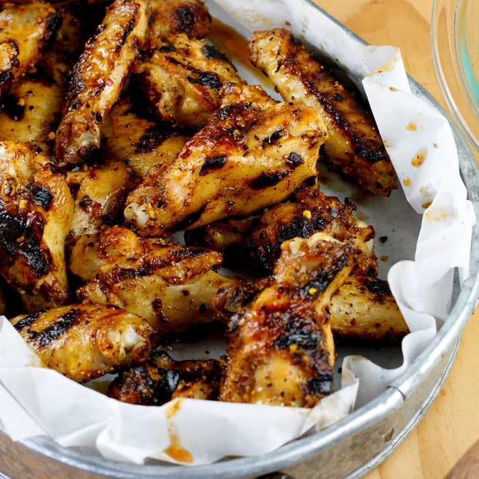 A close-up of a metal pan with a white paper liner filled with grilled chicken wings.