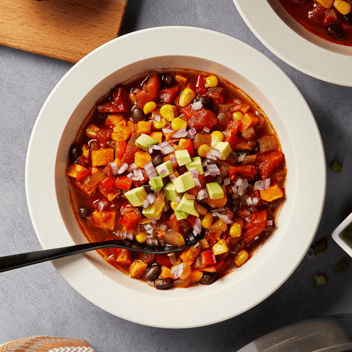 A white bowl filled with a hearty chili topped with avocado and red onion.