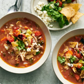 Two bowls of hearty soup with tortilla chips and salad on a light surface