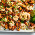 Platter of shrimp and sweet potatoes with green onions and lime wedges on a white background