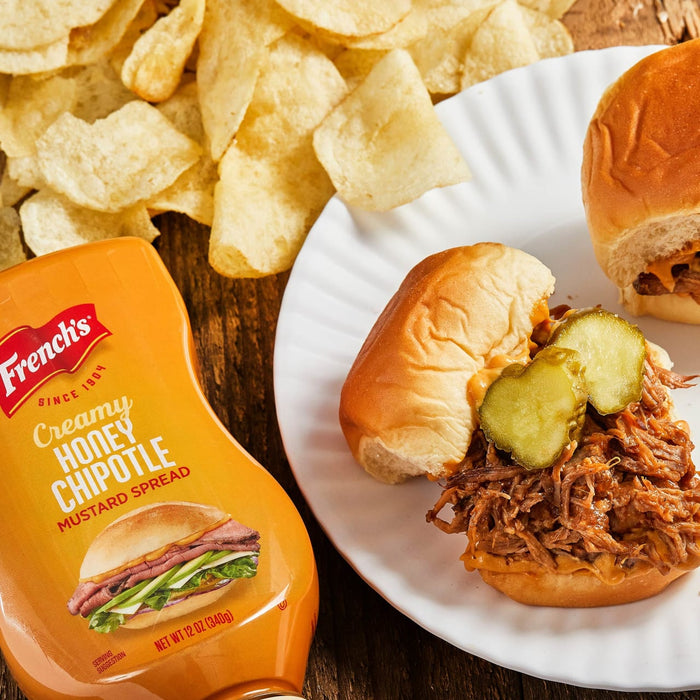 A bottle of Frenchs Creamy Honey Chipotle Mustard Spread next to a plate of pulled pork sliders with pickles.