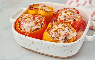 Stuffed bell peppers with melted cheese in a speckled baking dish on a light background