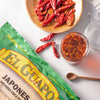 A bag of El Guapo Japanese Chile Powder with dried red chili peppers and chili oil in the background.