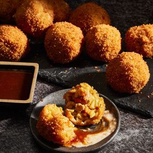 Golden brown fried rice balls are served on a dark slate platter alongside a small dish of dipping sauce and one ball broken open to reveal a savory filling of rice and vegetables.