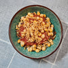 A vibrant bowl of koshary featuring layers of rice, lentils, and pasta topped with a rich tomato sauce, chickpeas, and crispy fried onions.
