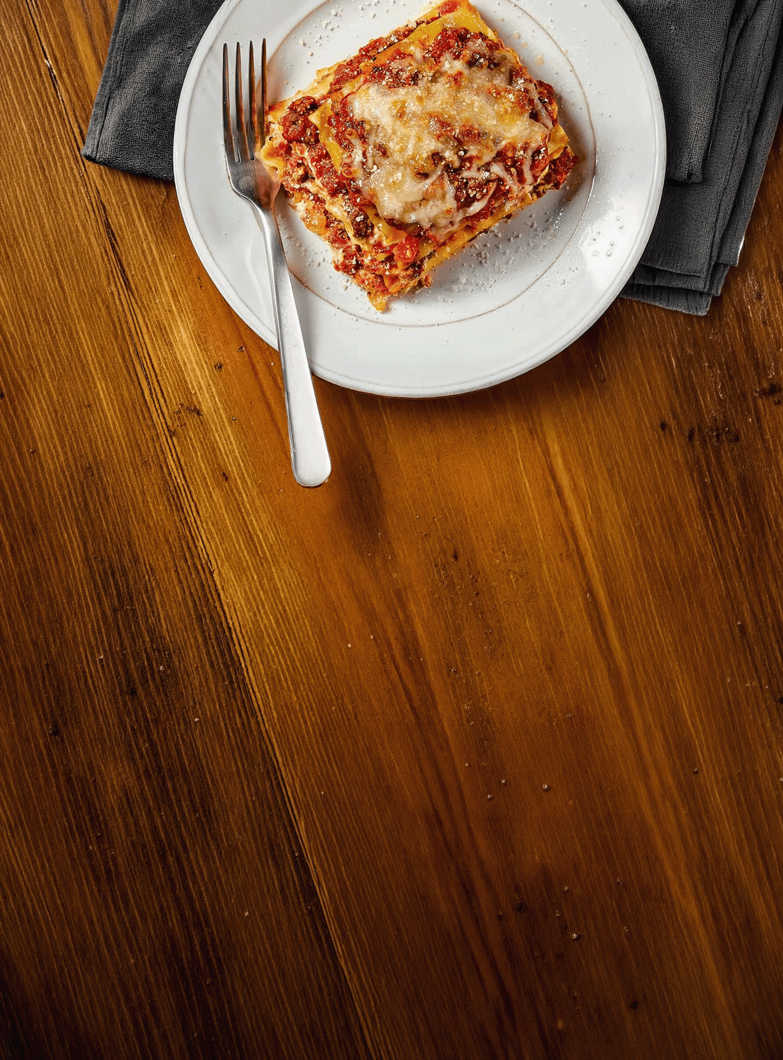 Slice of lasagna on a white plate placed on a wooden table