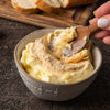A bowl of butter with a sprinkle of powder on top, being stirred with a wooden spoon.