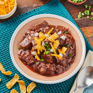 A bowl of chili topped with shredded cheese, tortilla chips, and green onions.