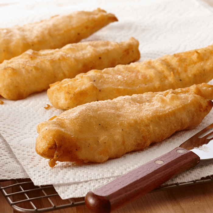 Four pieces of fried fish on a white paper towel with a wooden handled fork.