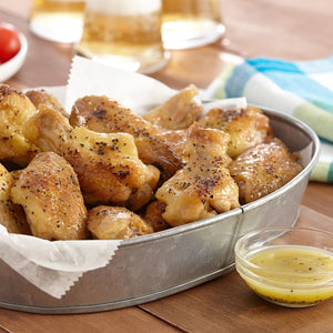 A metal bowl filled with roasted chicken wings and a small bowl of dipping sauce.