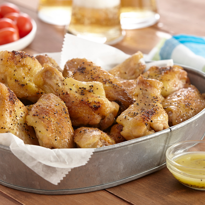 A metal bowl filled with crispy chicken wings and a small bowl of dipping sauce.