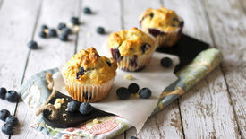 Blueberry muffins on a wooden table with scattered blueberries