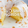 A close-up of a coconut cake with a white glaze and the text Two Simple Ingredients on top.