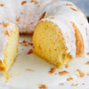 A close-up of a lemon cake with a white glaze and coconut flakes.