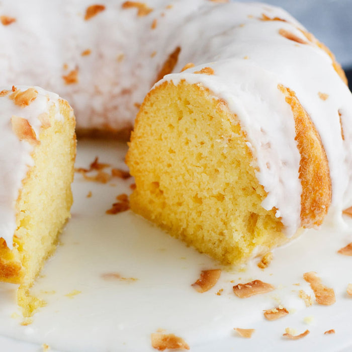 A close-up of a lemon cake with a white glaze and coconut flakes.