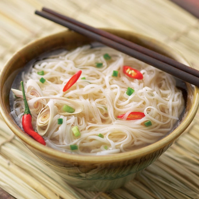 A bowl of Asian noodle soup with chili peppers and chopsticks resting on top.