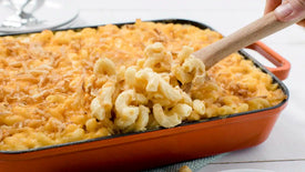 Macaroni and cheese being stirred with a wooden spoon in an orange baking dish.