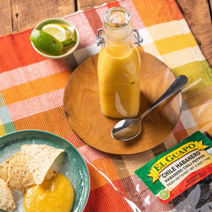 A bottle of El Guapo Chile Habanero hot sauce with a bowl of tortilla chips and a bowl of lime wedges.