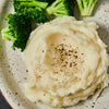 A plate of mashed potatoes with black pepper and broccoli florets.